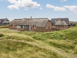 Et traditionelt bindingsværkshus med stråtækt tag, murstensfacade, en træbænk og et græsfuldt landskab.