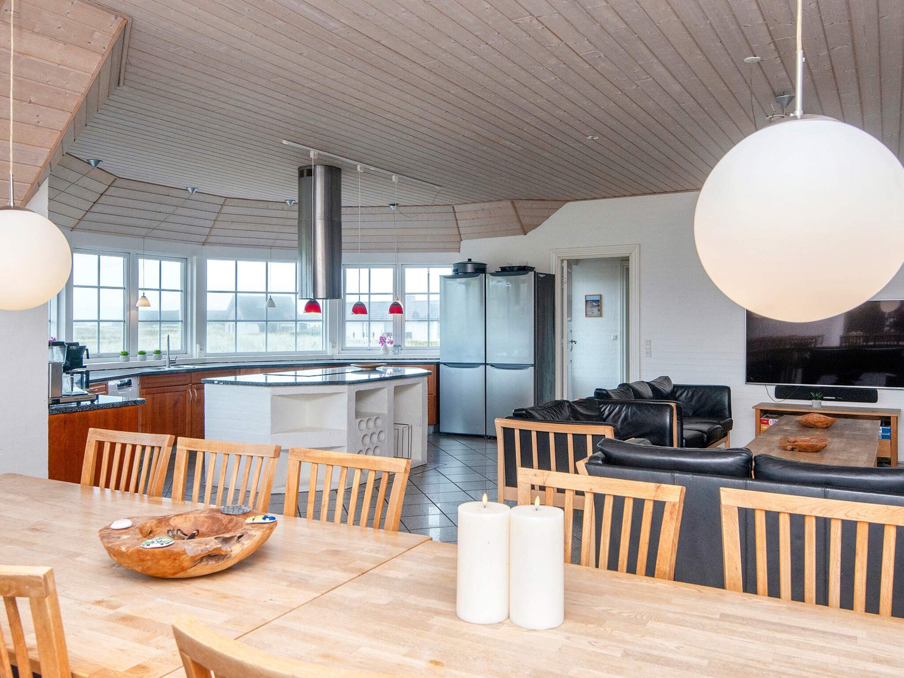 A modern kitchen with a dining area, featuring a large island, wooden furniture, and a flat-screen TV.