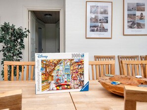 Una mesa de comedor con una caja de rompecabezas de Disney Ravensburger, sillas de madera y un cuenco de madera con un posavasos.