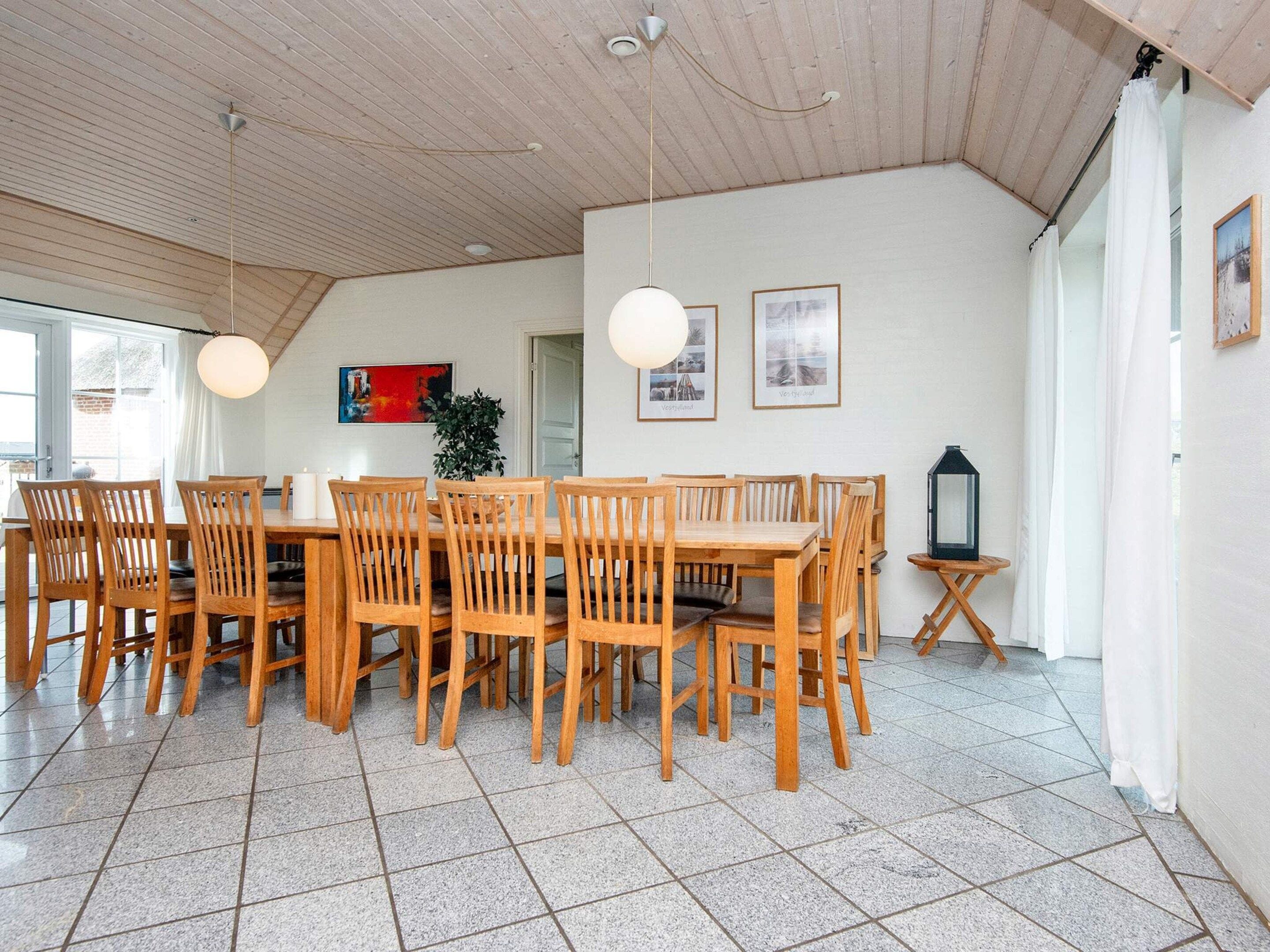 A dining area with wooden tables and chairs, a potted plant, and framed pictures on the wall.