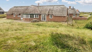 A thatched-roof house with a brick exterior, a wooden bench, and a swing set in a grassy field. - 4 Star Holiday Home in Harboore (Harboore)
