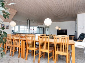 A modern dining area with wooden tables and chairs, a large window, and a flat-screen TV. - 4 Star Holiday Home in Harboore (Harboore)