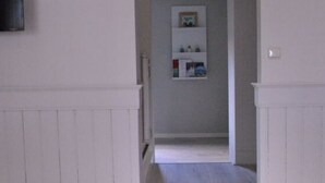 En gang med en hvid dør, der fører til et rum med et hvidt skab og en lille reol med bøger.