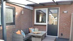 En terrasse med fletmøbler, et bord og en dør.