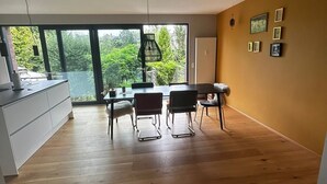 A modern living room with a dining area, large windows, and a view of greenery. - Oasis of peace near the city center: Stylish garden apartment, 2 bedrooms, top public transport links  (Düsseldorf)