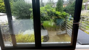 A room with a large sliding glass door leading to a balcony with a metal railing and a view of greenery and buildings. - Oasis of peace near the city center: Stylish garden apartment, 2 bedrooms, top public transport links  (Düsseldorf)