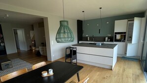 A modern kitchen with white cabinets, a black countertop, and a hanging green pendant light. - Oasis of peace near the city center: Stylish garden apartment, 2 bedrooms, top public transport links  (Düsseldorf)