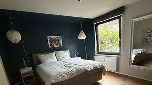 A bedroom with a bed, wooden flooring, a window with a view, and a ceiling light. - Oasis of peace near the city center: Stylish garden apartment, 2 bedrooms, top public transport links  (Düsseldorf)