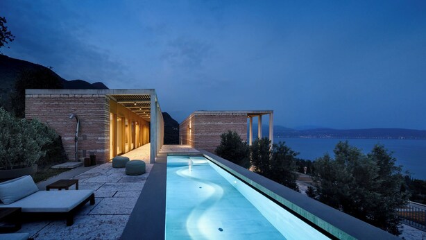 Un espace piscine extérieur moderne avec vue sur la mer, comprenant une longue piscine, des chaises longues et un espace salon couvert.