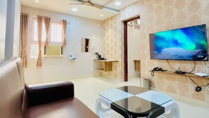 A modern living room with a sofa, a glass coffee table, a ceiling fan, a TV, and a patterned wall. - Magan Enclave (Tarangambadi)
