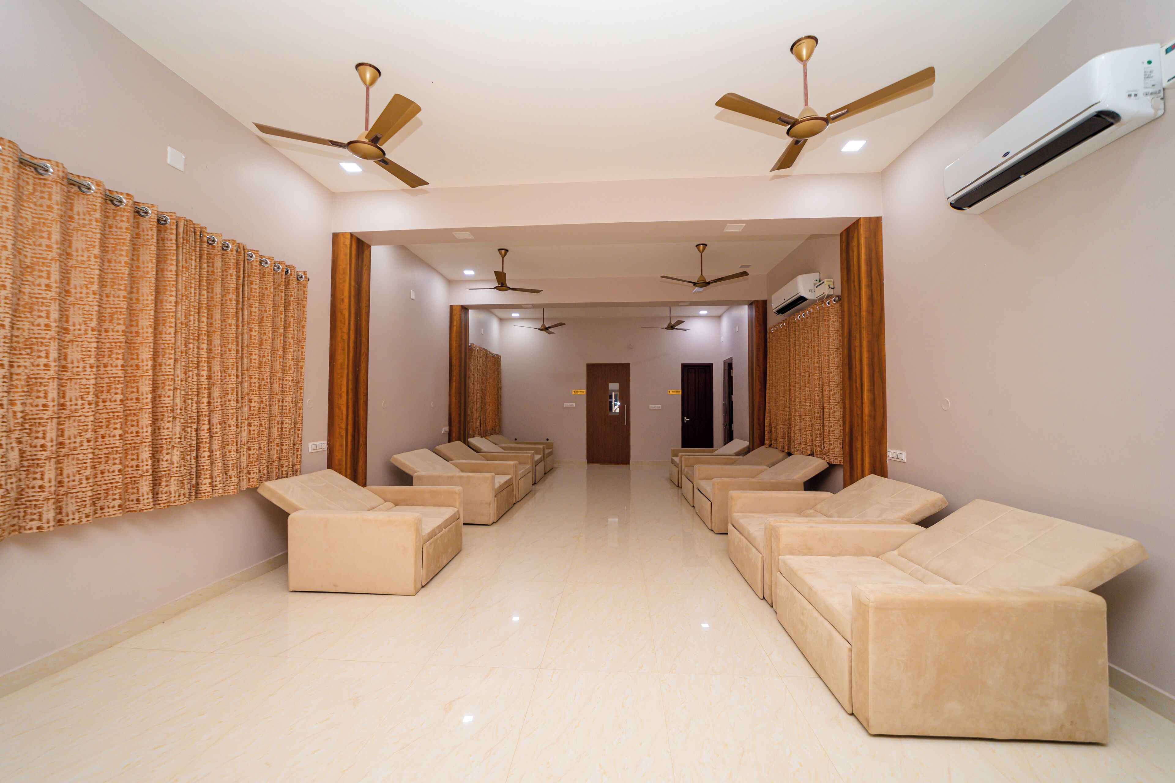 A hotel lobby with a row of beige sofas, ceiling fans, and an air conditioning unit.