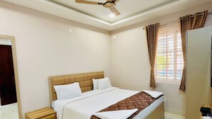 A bedroom with a bed, a nightstand, a ceiling fan, a window with curtains, and a wardrobe. - Magan Enclave (Tarangambadi)