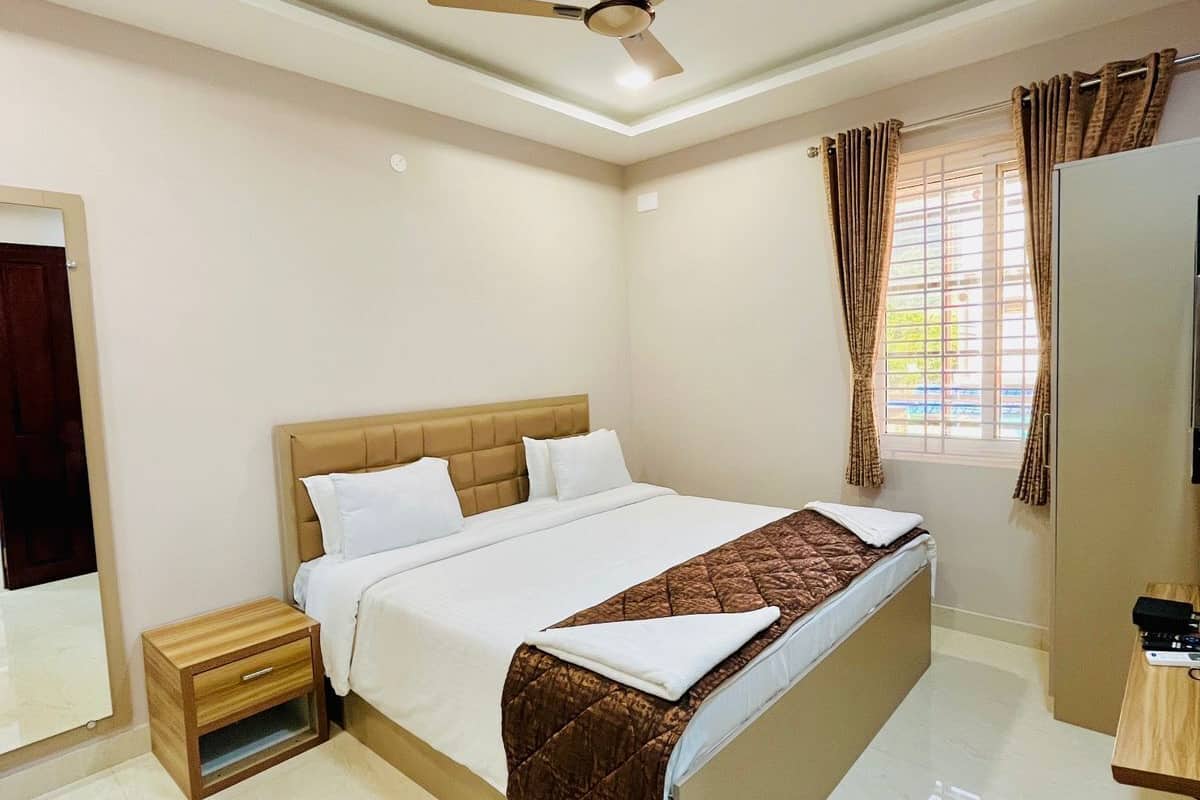 Une chambre à coucher comprenant un lit, une table de chevet, un ventilateur de plafond, une fenêtre avec des rideaux et une armoire.
