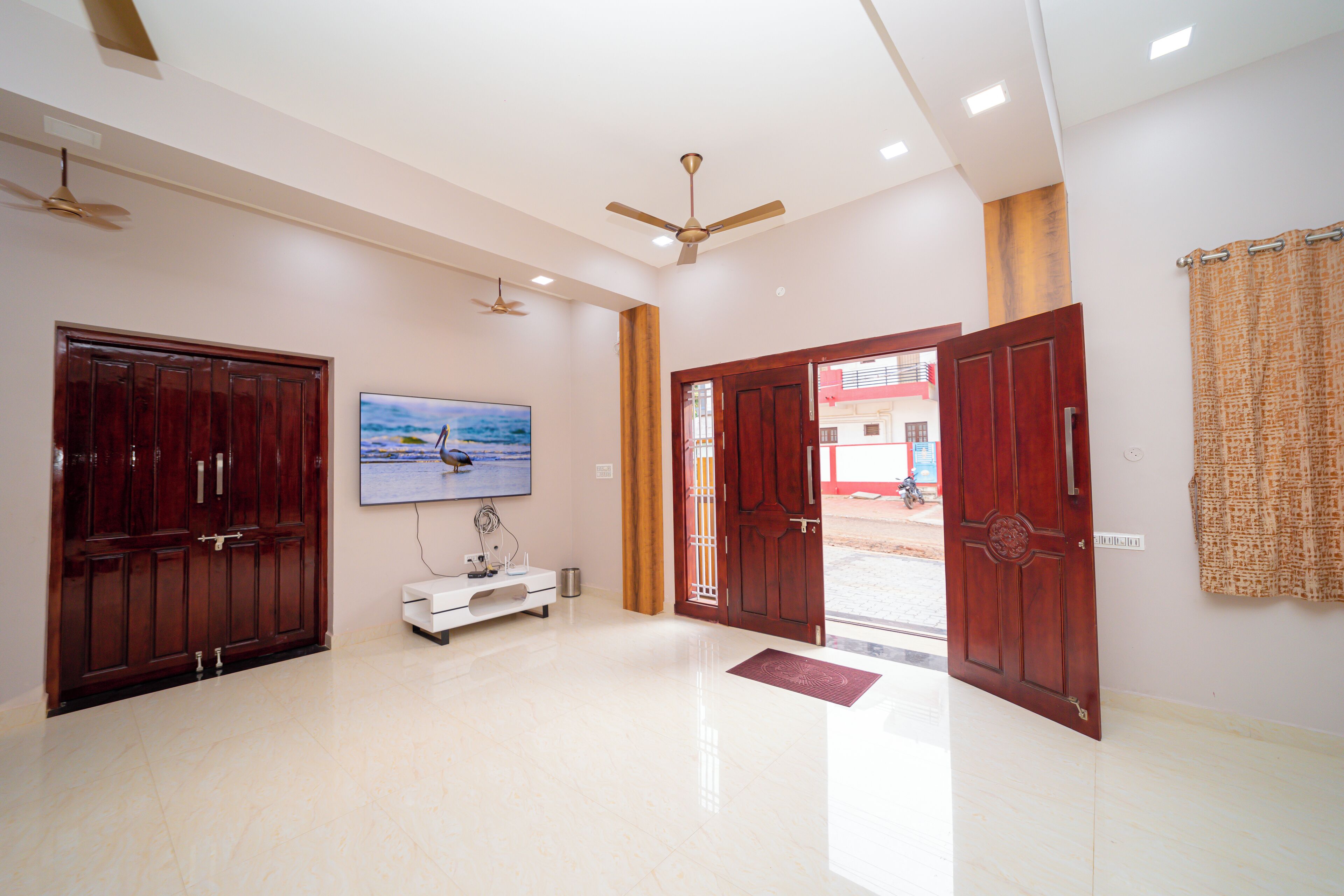 A spacious lobby with a tiled floor, a television mounted on the wall, and two wooden doors.