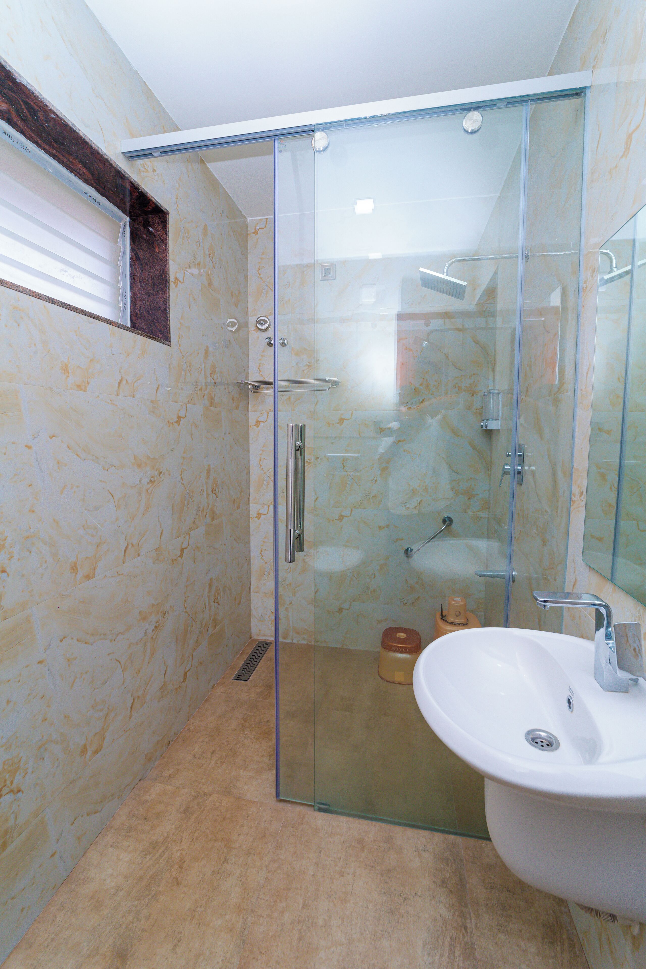 Un baño moderno con ducha envuelta en vidrio, un lavamanos blanco y paredes de mármol.