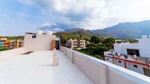 A rooftop terrace with a view of surrounding buildings and mountains. - Magan Enclave (Tarangambadi)