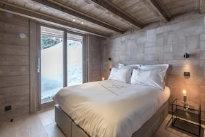 Ein Schlafzimmer mit einem großen Bett, Holzbalkendecke, Steinwänden und Blick auf eine verschneite Landschaft.