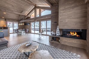A spacious living area with a fireplace, wooden furniture, and large windows. - Chalet, terrace, fireplace or stove, tv, ski locker, 193m², La Clusaz (La Clusaz)