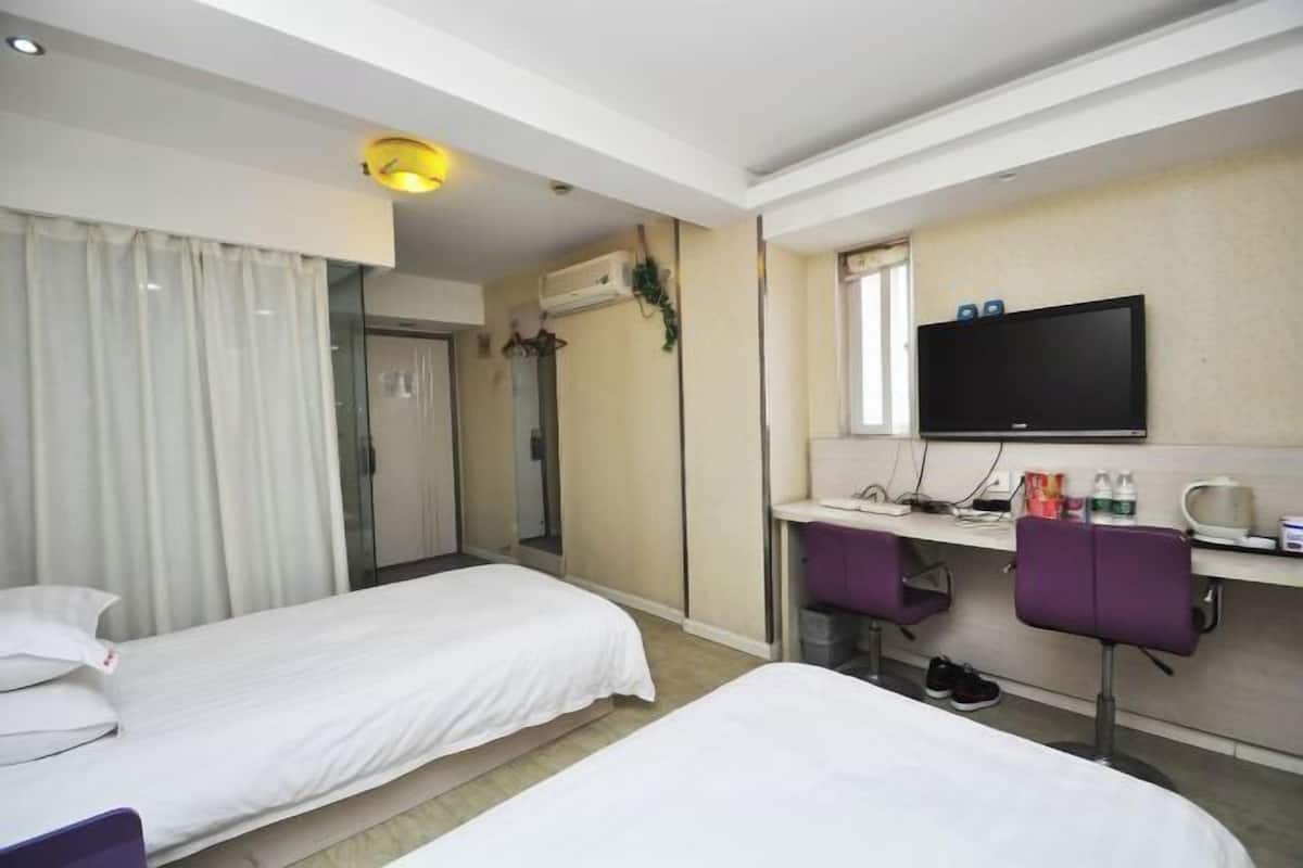 Hotellihuone, jossa on kaksi erillistä sänkyä, työpöytä tietokoneella, televisio ja pieni oleskelualue tuoleineen.