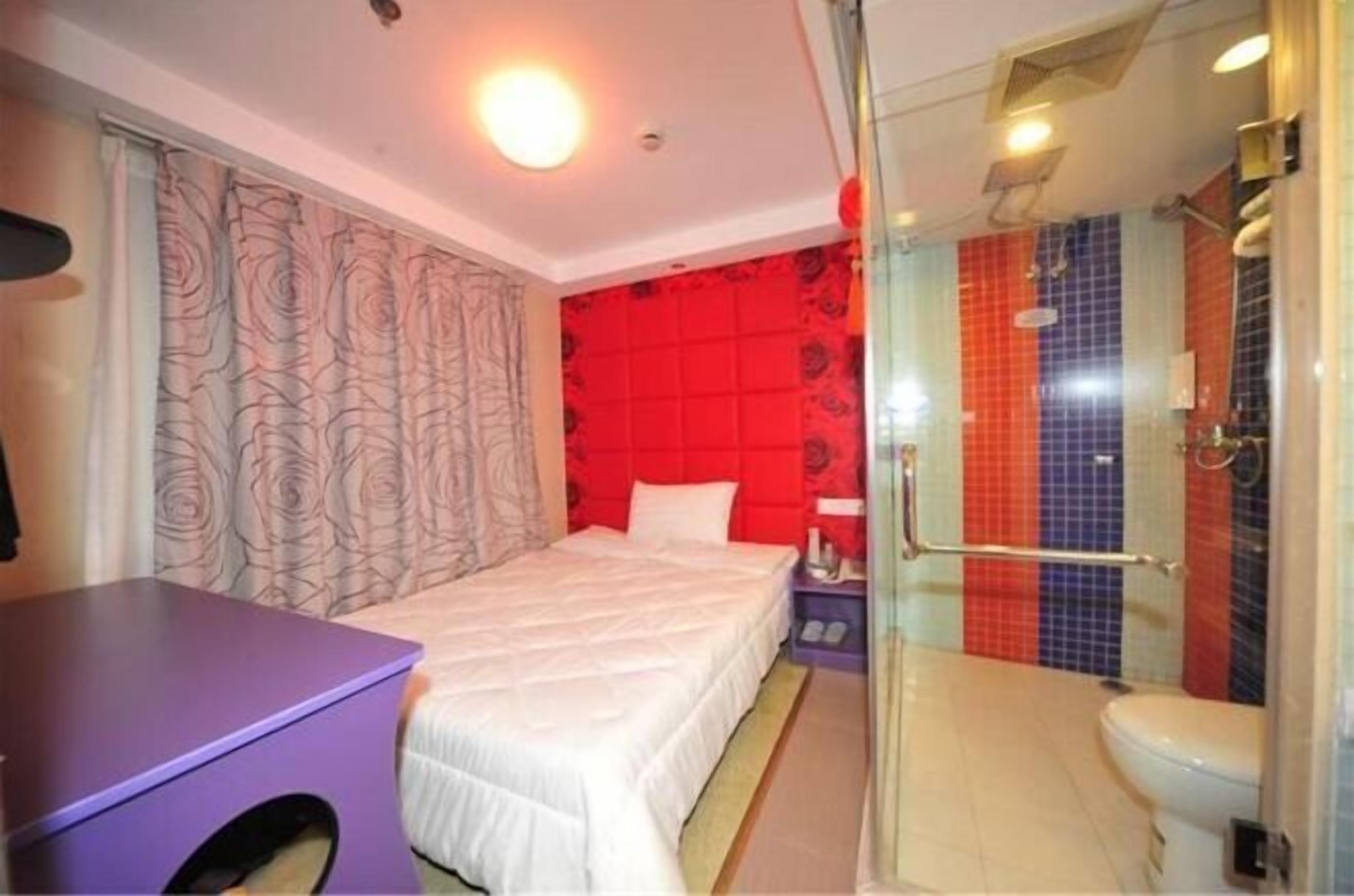 A hotel room with a bed, a desk, a shower with colorful tiles, and a glass-enclosed bathroom.