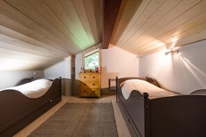 Un dormitorio con dos camas, un aparador de madera, un ventanal y una lámpara fijada a la pared.