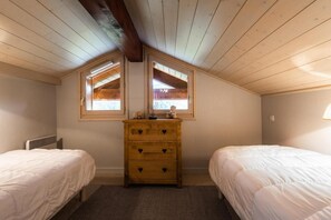 A bedroom with two beds, a wooden dresser, and two windows.
