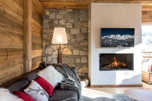 Um quarto aconchegante com parede de pedra, lareira, sofá com manta e TV na parede.