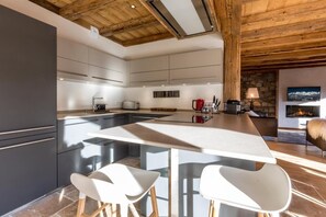 Uma cozinha moderna com uma ilha central, banquetas e uma lareira de pedra na sala de estar.