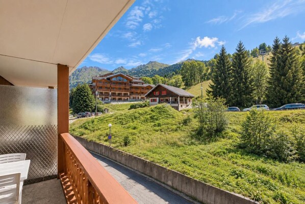 A hotel with a balcony overlooking a mountainous landscape, a parking area with several cars, and a building with a wooden facade.