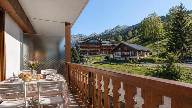 A balcony with a table set for breakfast, overlooking a mountain resort with wooden buildings. - 300m from ski slopes, 2nd floor, view mountain, balcony, fireplace or stove, tv, ski locker, 53m² (La Clusaz)