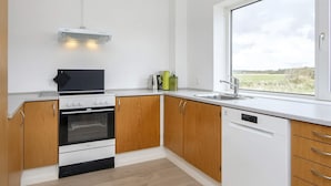 Una cocina moderna con armarios de madera, horno empotrado, lavavajillas y ventana con vistas al campo.