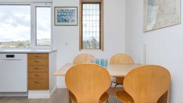 Una cocina moderna con lavavajillas, armarios de madera, una mesa de comedor con cuatro sillas y un ventanal.