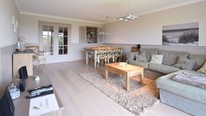A spacious living area with a sofa, a coffee table, and a dining table with chairs. - Golf en Strand Apartment Near the Beach (De Haan)