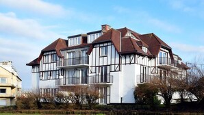 A multi-story residential building with a symmetrical facade, large windows, and balconies. - Golf en Strand Apartment Near the Beach (De Haan)