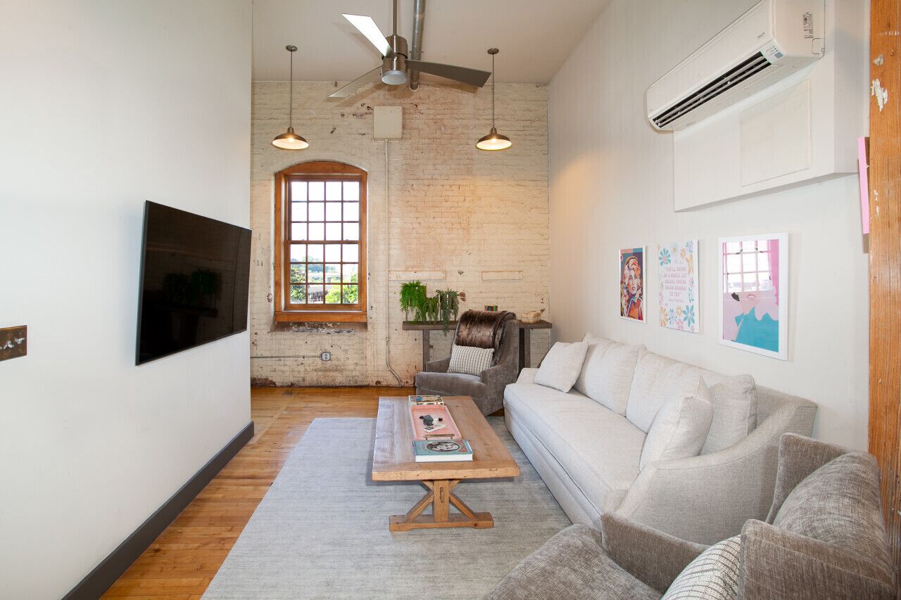 A modern living room with a large window, a flat-screen TV, a wooden coffee table, and a gray sofa.