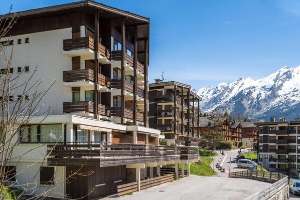 A multi-story hotel with balconies, a parking area, and a view of snow-capped mountains.