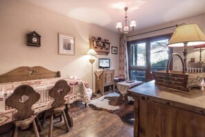 A cozy room with a wooden bed, a dining table with chairs, a small desk, and a lamp.
