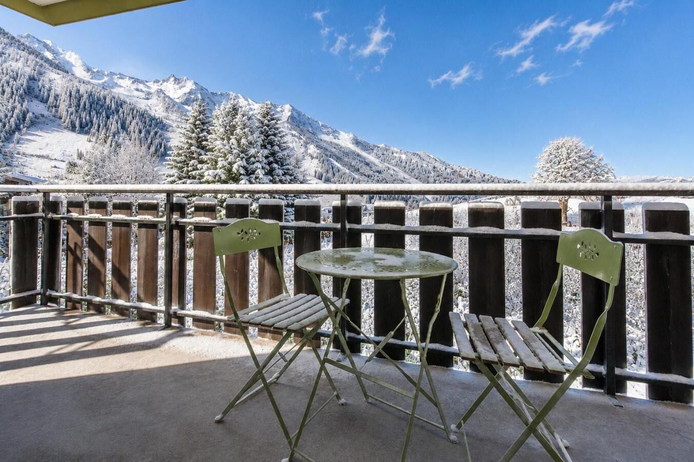 Un balcón con mesa y sillas, con vistas a un paisaje montañoso nevado.