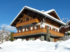 A multi-story wooden chalet with balconies, surrounded by snow.