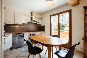 A modern kitchen with a dining table and chairs, a dishwasher, and a large window with a view of greenery.