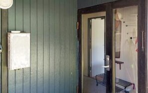 Ein Zimmer mit Holztür, kleinem Fenster und einer Bank vor der Tür.