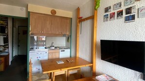 A compact living space with a kitchenette, wooden furniture, and a flat-screen TV mounted on the wall.