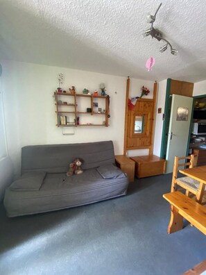 Uma sala de estar com um sofá cinza, prateleiras de madeira, uma mesinha e uma cadeira de madeira.
