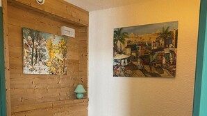 A room with a wooden wall, a bed with a quilt, and two paintings.