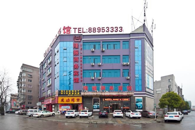 A multi-story hotel with a prominent red sign on the facade, a visible telephone number, and several parked cars in front.