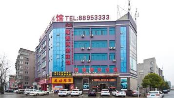 A multi-story hotel with a prominent red sign on the facade, a visible telephone number, and several parked cars in front.