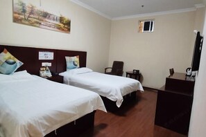 Una habitación de hotel con dos camas individuales, un escritorio, una silla, un ventanal pequeño y un cuadro en la pared.