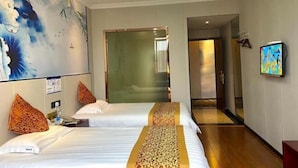 Ein Hotelzimmer mit zwei Betten, einem großen floralen Wandbild, einem Fernseher und einem Flur, der zu einem weiteren Zimmer führt.