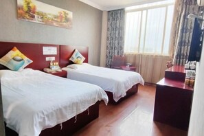 Habitación de hotel con dos camas, un escritorio y una ventana con cortinas.