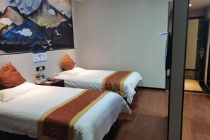 Habitación de hotel con dos camas, cada una con ropa de cama blanca y un detalle decorativo marrón. En la pared detrás de las camas, hay un cuadro de montañas.